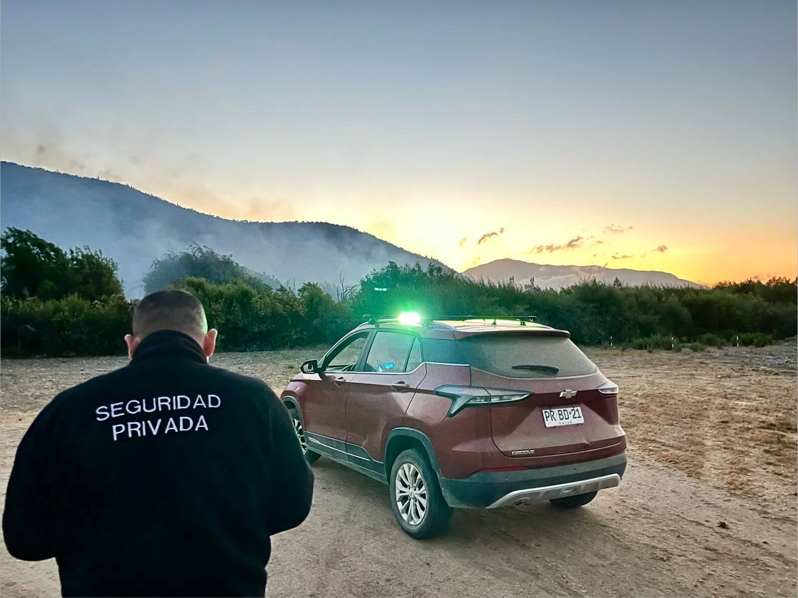 Vehículo de seguridad rojo respondiendo en entorno rural/agrícola con humo de fondo - Valcop